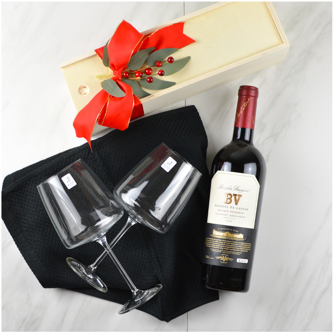 Wooden slide wine box with holly, a bottle of wine, two wine glasses and a black kitchen towel