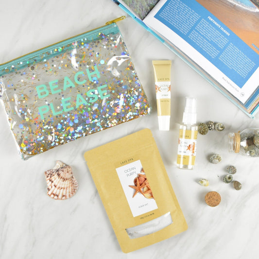 vinyl and glitter makeup bag with "Beach Please" on it, jar of sea shells, ocean scented scrub salts, ocean scented lip balm, ocean scented linen spray