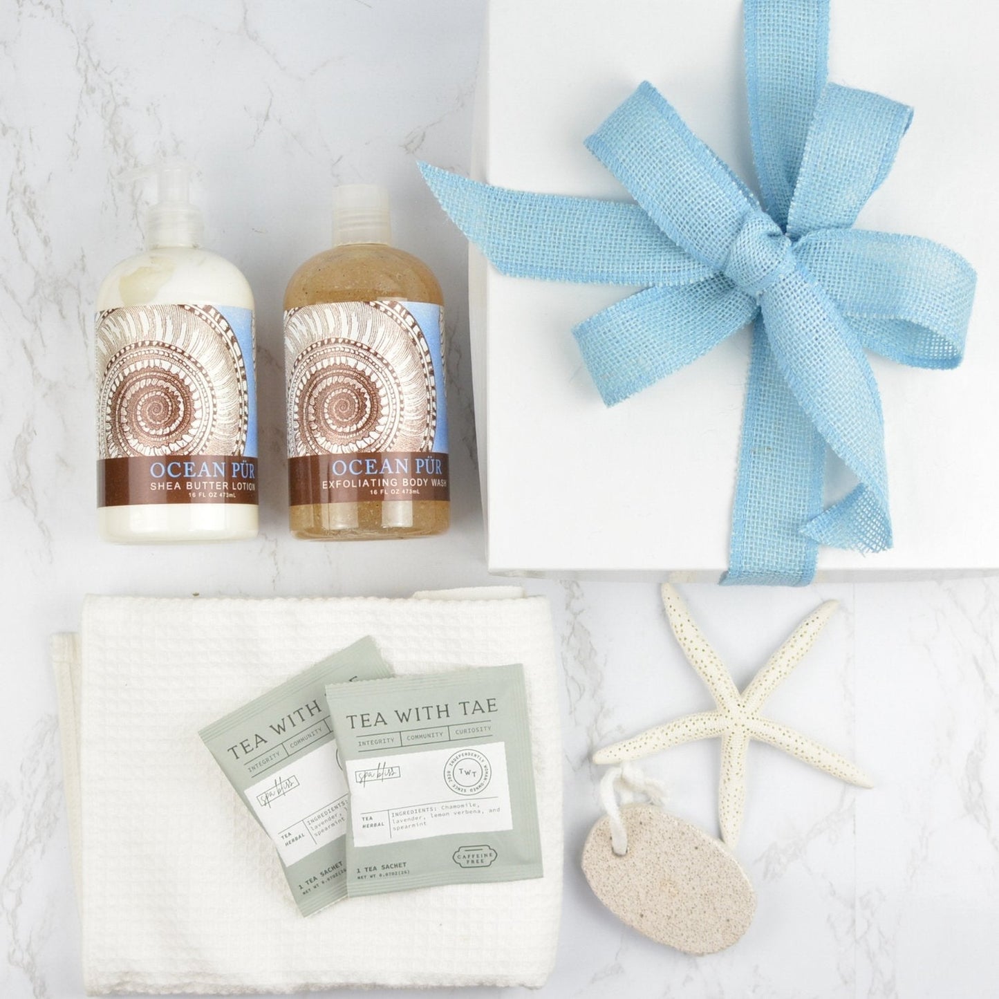 White gift box with bow, ocean scented body wash, ocean scented lotion, two individually wrapped Tea wth Tae tea bags, white hand towel, pumice stone and sea star